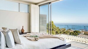 Ein Schlafzimmer mit einem großen Bett, weißer Bettwäsche und Blick auf den Ozean.