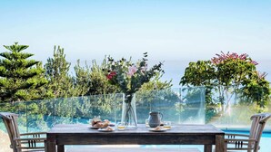 Ein Holztisch mit Blumen, einer Karaffe und Gläsern, mit Blick auf einen Pool und die umliegende, grüne Vegetation.