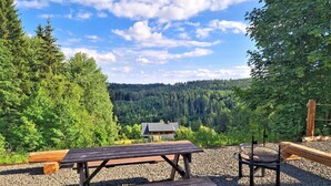 Piknikalue, jossa on puinen pöytä ja penkit, ja jonka ympärillä on soraa. Taustalla näkyy metsäinen vuorimaisema.