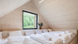 Un dormitorio con techo inclinado, un ventanal grande y una cama con toallas ordenadas.