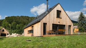 Una cabaña de madera con techo inclinado, ventanas grandes y chimenea.