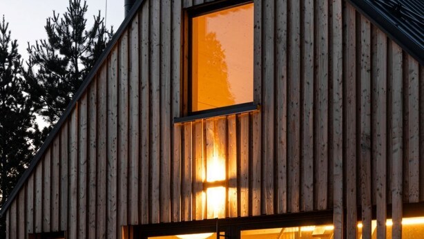 Una cabaña de madera con un ventanal grande, una escalera que da al interior y una terraza.