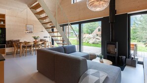 Ein modernes Wohnzimmer mit einem grauen Sofa, einer Holztreppe und einem großen Fenster mit Blick ins Freie.