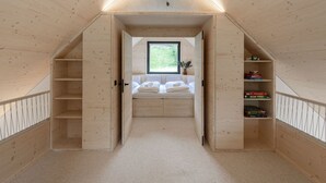 Ein Schlafzimmer im Dachgeschoss mit Holzboden, schrägen Wänden, einem Fenster, einem Bett und eingebauten Regalen.