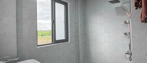 A modern bathroom with a large window, a freestanding bathtub, a shower, and a toilet.
