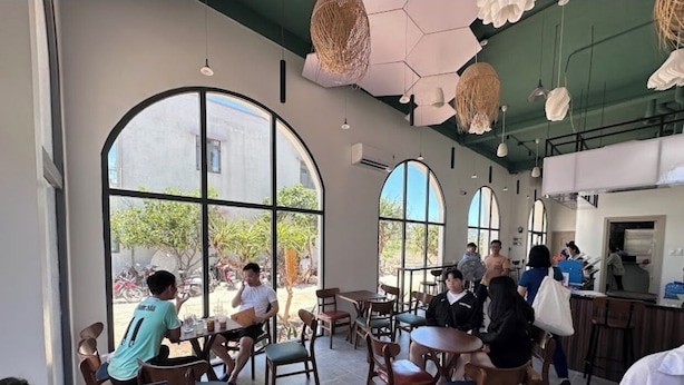 A cafe with large arched windows, wooden tables, and hanging light fixtures. - Nang Hotel - Phu Quy (Phu Quy)