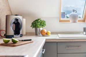 Et køkken med kaffemaskine, en potteplante, en skål med frugt og et vindue med udsigt.
