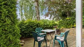Une terrasse en bois avec deux chaises turquoise et une table, entourée d’une végétation luxuriante et d’arbres.