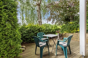Eine Holzterrasse mit zwei türkisfarbenen Stühlen und einem Tisch, umgeben von üppigem Grün und Bäumen.