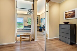 A hallway with a wooden bench, a black storage unit, and a view of a balcony with a bed.