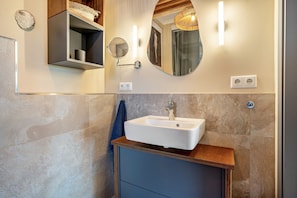 A bathroom with a white sink, a mirror, a towel rack, and a shelf with a basket.