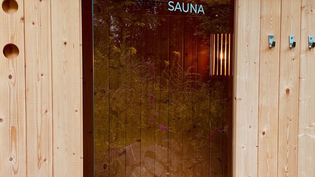 Un cuarto de sauna con paredes de madera, un banco y una puerta de cristal con la palabra 'SAUNA' visible.