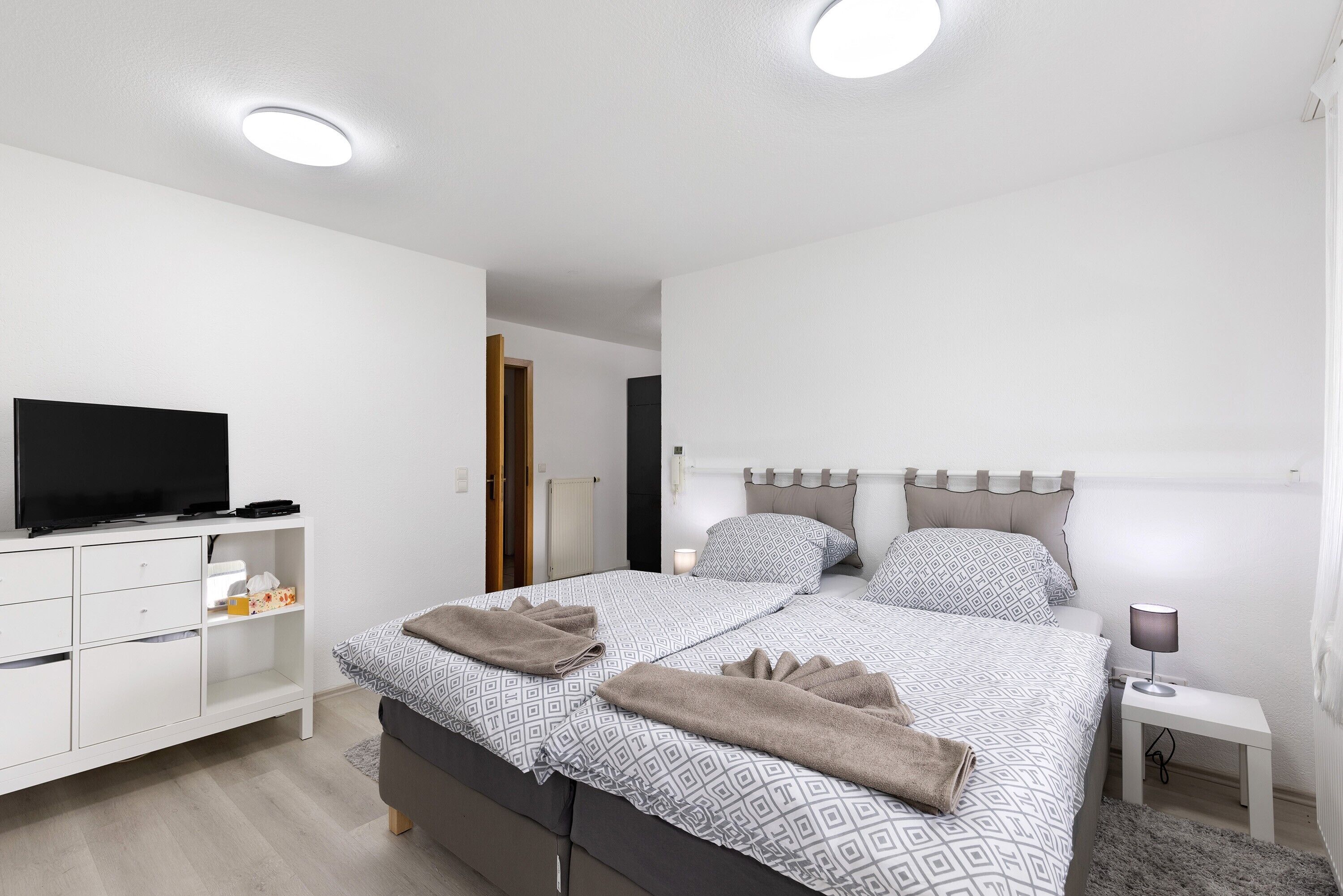 Een moderne slaapkamer met een bed, nachtkastje, televisie en een garderobe.