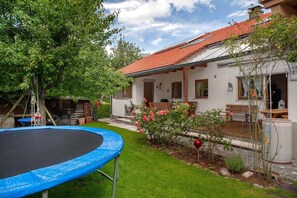Una casa con techo de tejas rojas, un trampolín y un jardín con flores.