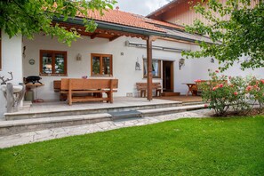 Una casa con un patio, bancos de madera, una parrilla y un jardín lleno de flores.