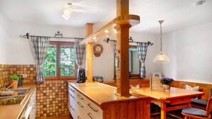 Una cocina con una isla de madera, un comedor con un banco y un ventanal con cortinas.