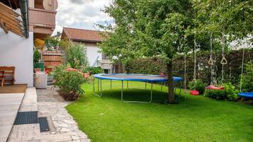 Un jardin avec un trampoline, un arbre et une balançoire.