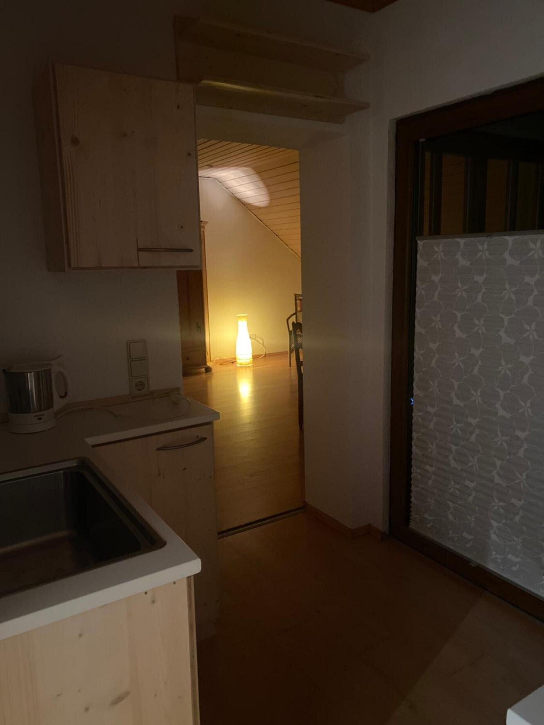A kitchen with wooden cabinets, a sink, and a countertop. There is a door leading to another room.