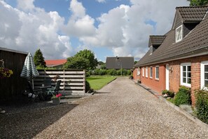 A gravel driveway leading to a house with a red brick exterior and a wooden fence.