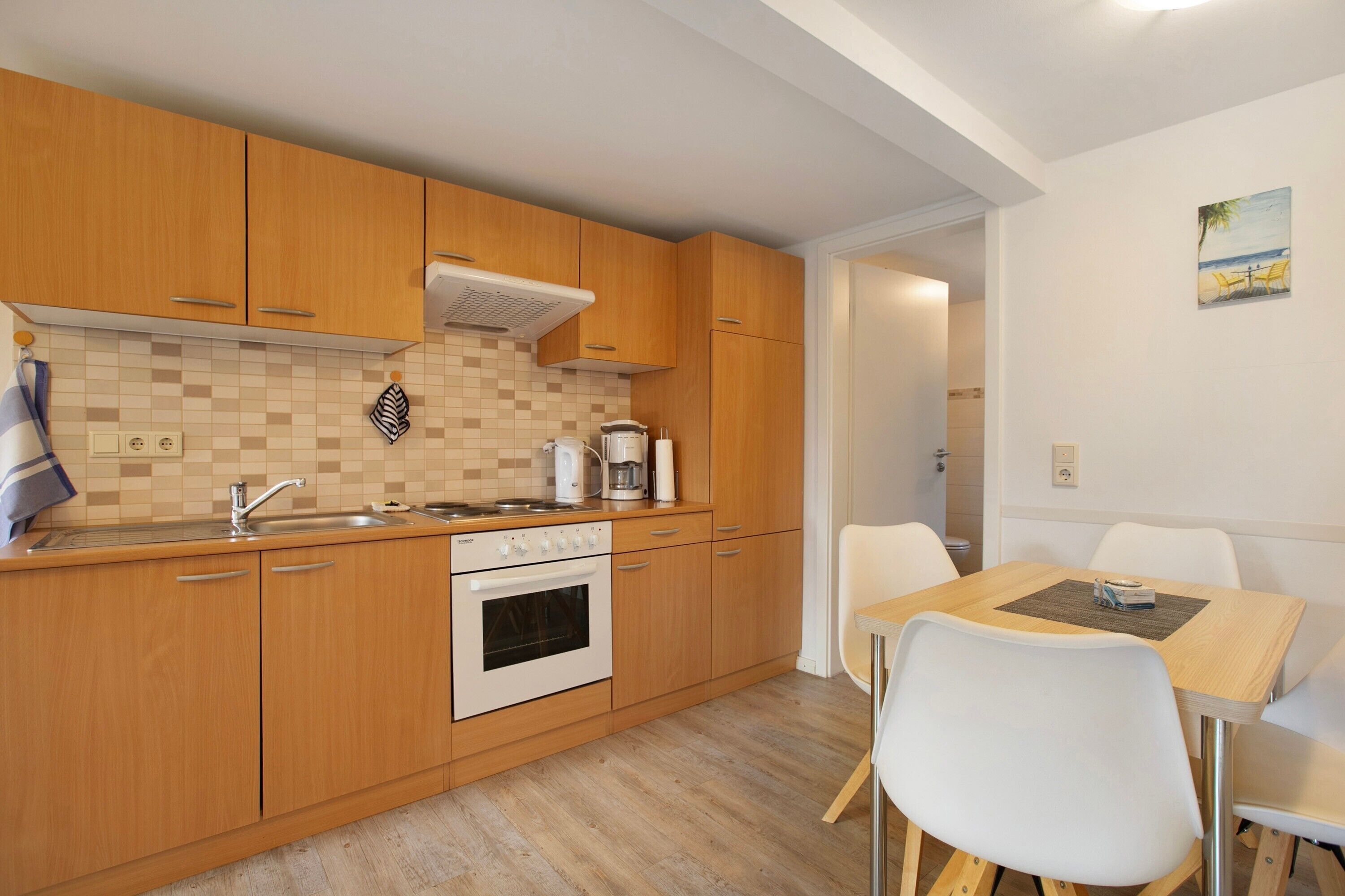 Une cuisine avec des meubles de rangement en bois, une cuisinière, un évier et une table à manger avec des chaises.