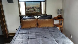 A bed with a grey quilt, two brown pillows, and a wooden nightstand with a lamp. - Windy Ridge Cabin
Babb/St.Marys (Babb)