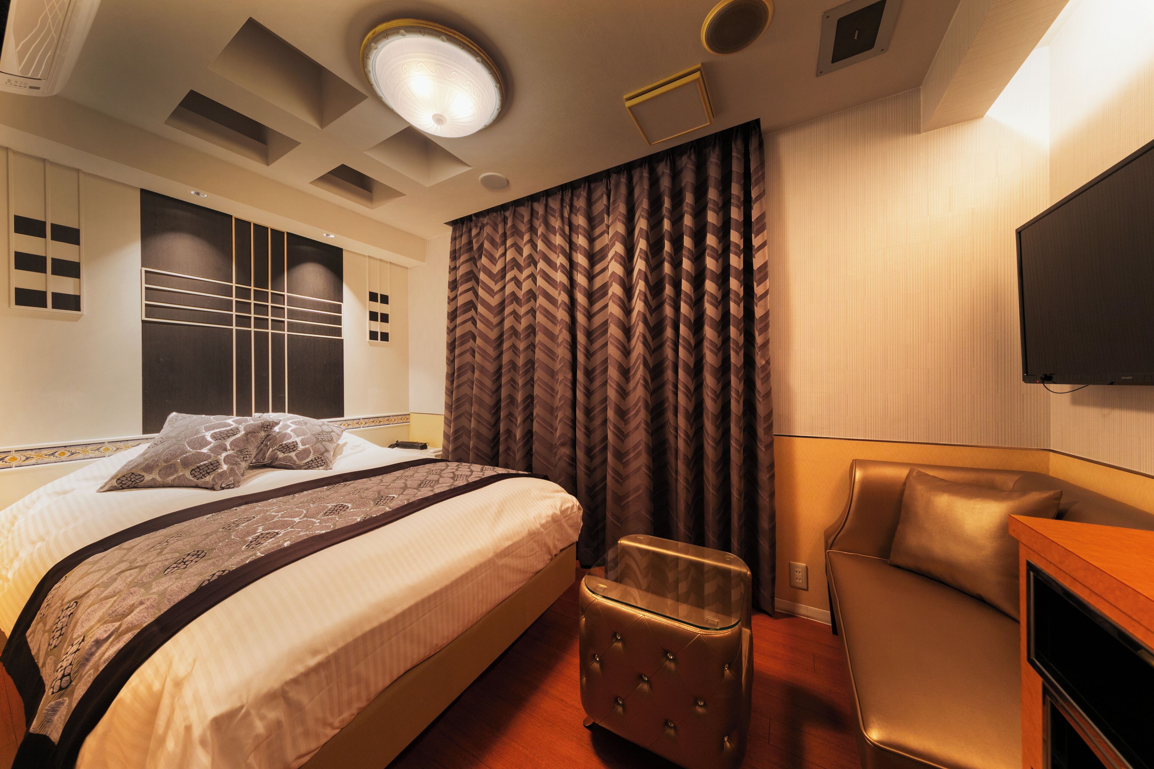 A hotel room with a bed, a small seating area, a television, and a large window with curtains.
