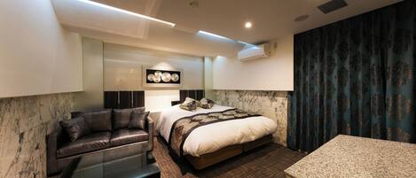 A modern hotel room with a bed, a sofa, a glass coffee table, and a marble accent wall.