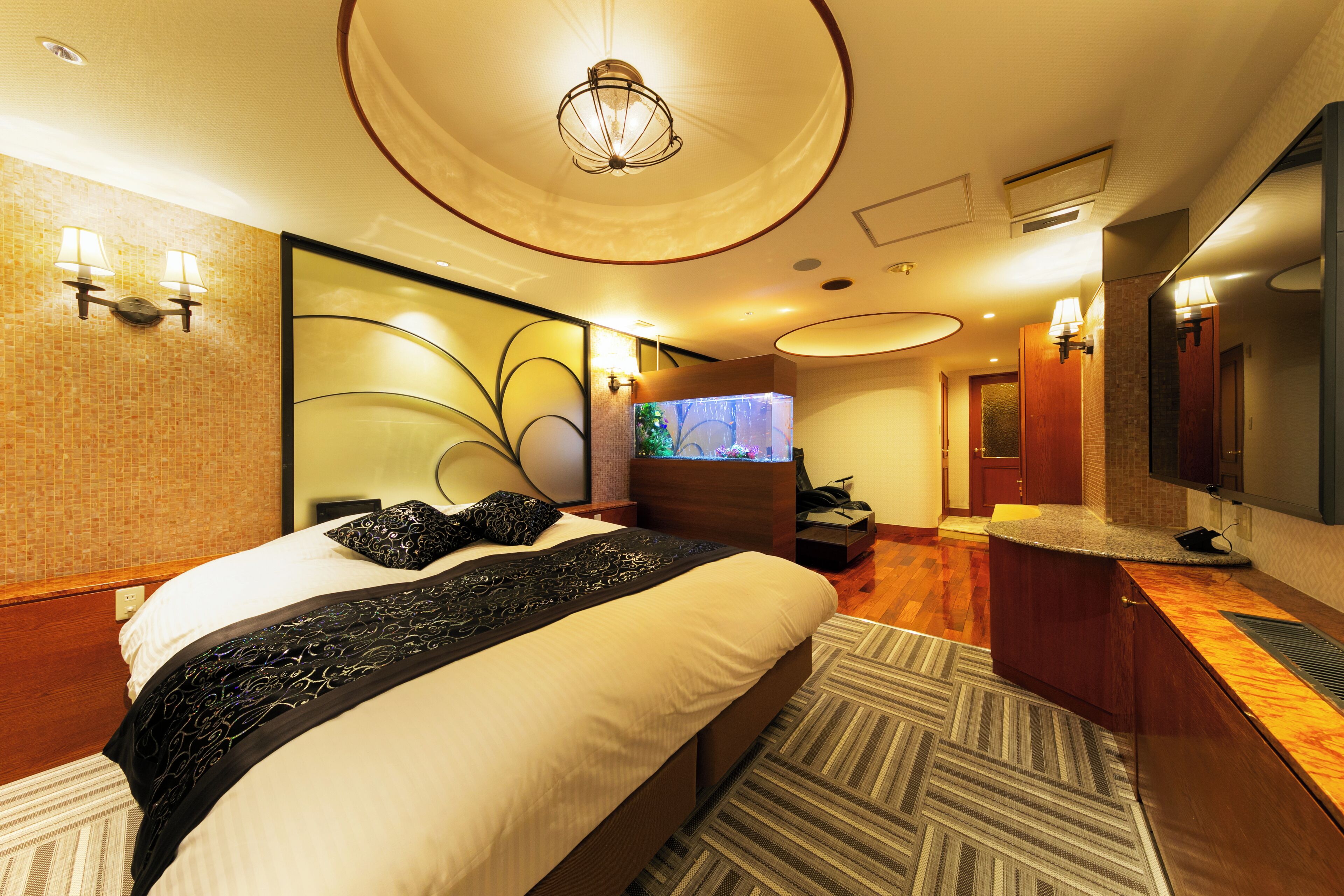 A modern hotel room with a large bed, a TV, a desk, and a bathroom with a mirror and sink.