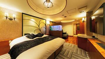 A modern hotel room with a large bed, a TV, a desk, and a bathroom with a mirror and sink.