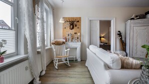 A room with a white sofa, a rocking chair, a white cabinet, and a wall-mounted deer head. - Apartment 'Ferienwohnung Stielbruch' with Private Terrace, Private Garden and Wi-Fi (Viöl)