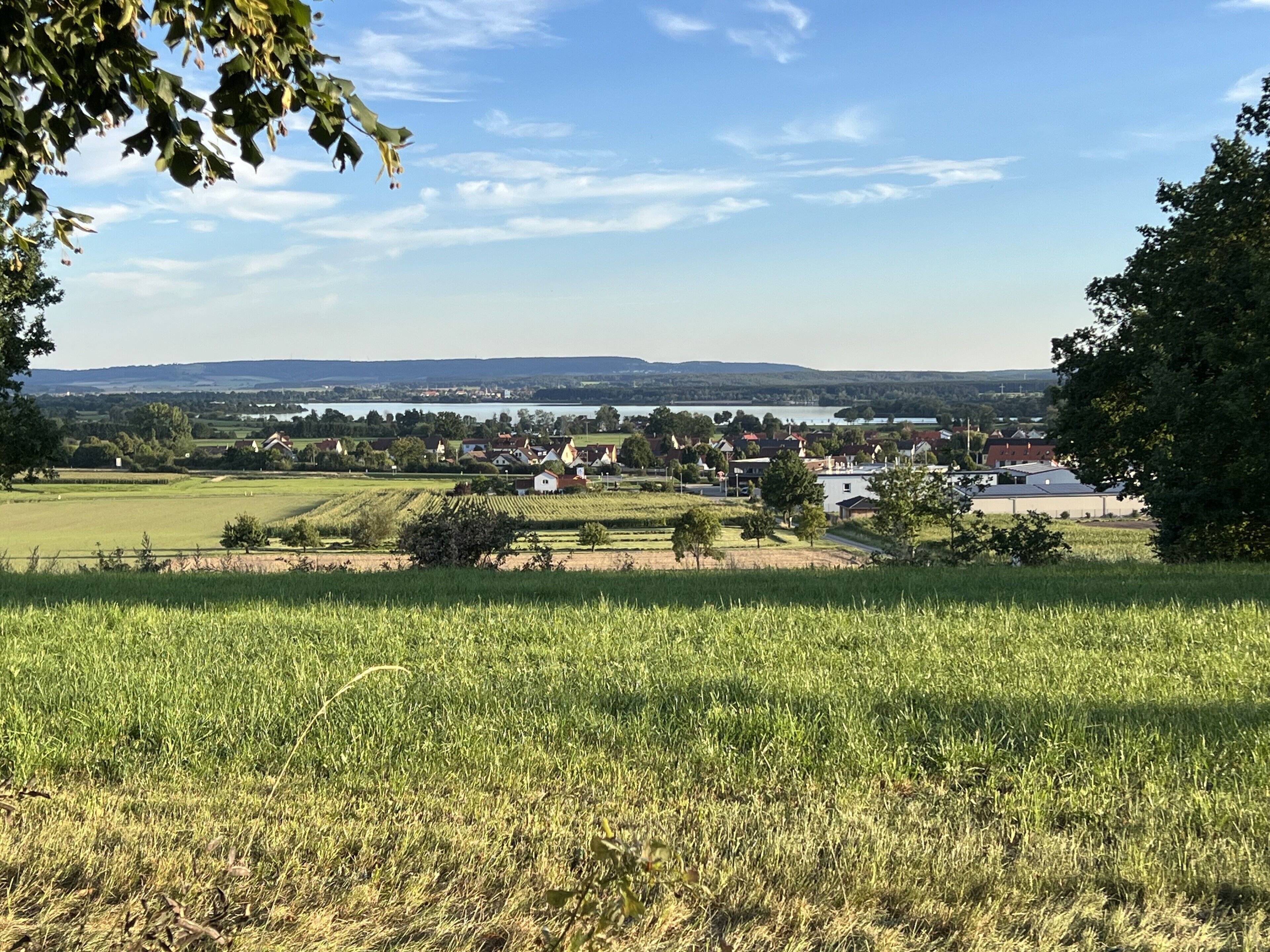 A rural landscape with fields, houses, and a distant body of water.