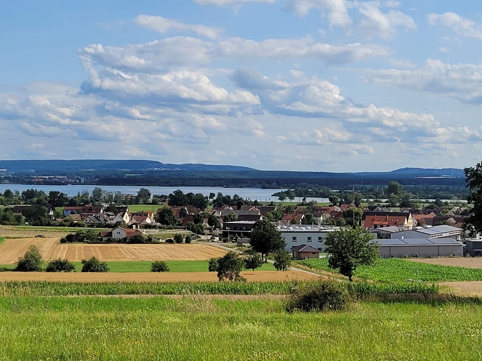 A rural landscape with fields, a village, and a lake.