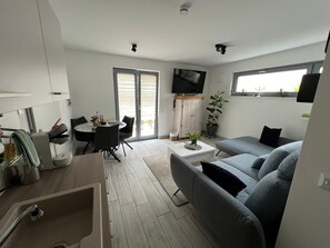 Ein modernes Wohnzimmer mit Essbereich, einer Couch, einem Fernseher und einer Schiebeglastür nach draußen.