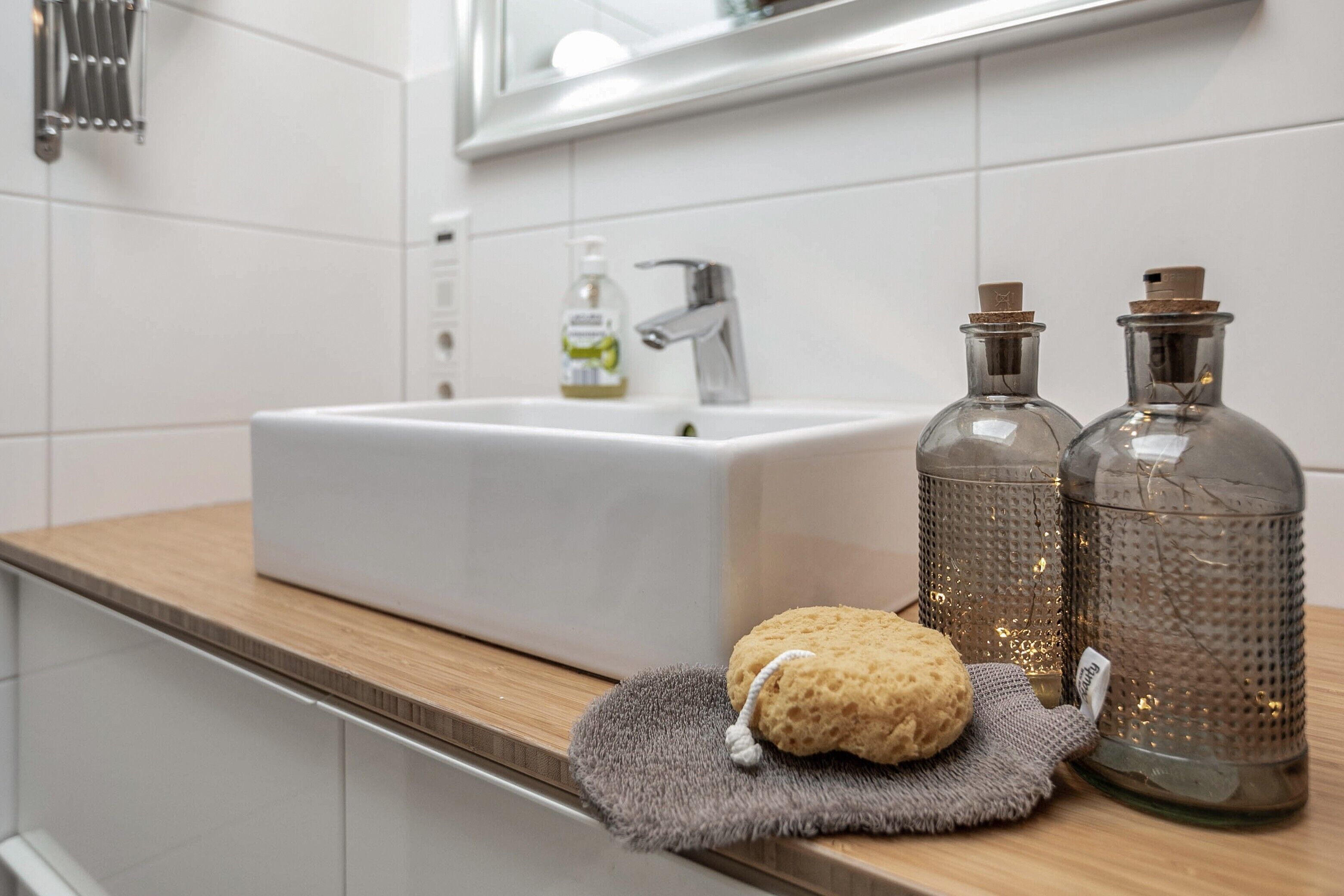 Ein Badezimmer mit einem weißen Waschbecken, zwei Glasflaschen, einem Schwamm und einem Handtuch auf der Ablagefläche.