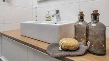 Ein Badezimmer mit einem weißen Waschbecken, zwei Glasflaschen, einem Schwamm und einem Handtuch auf der Ablagefläche.