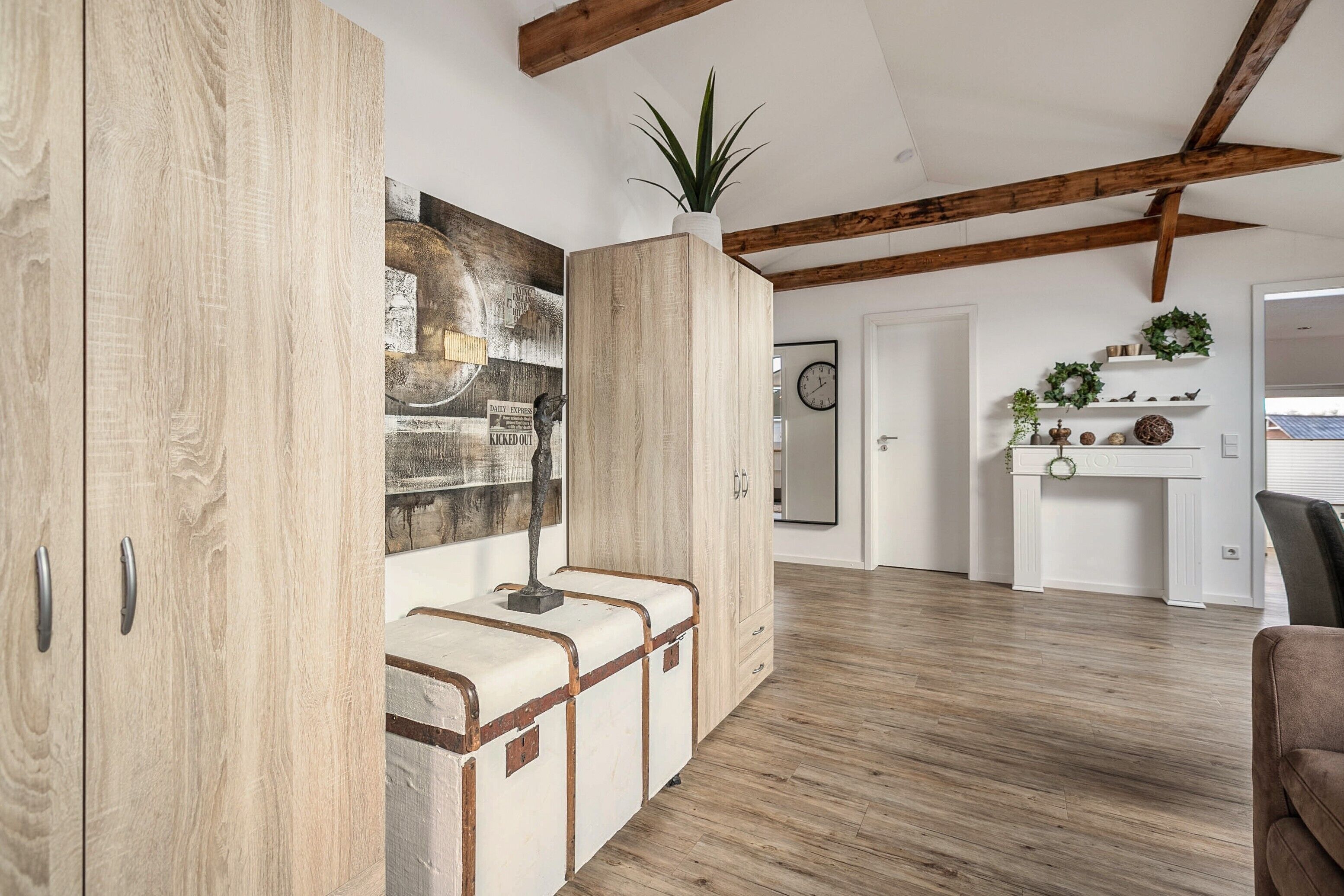 Ein Zimmer mit Holzboden, einem großen Holzschrank, einer Bank mit Pflanze darauf und einer Wand mit einem gerahmten Bild.