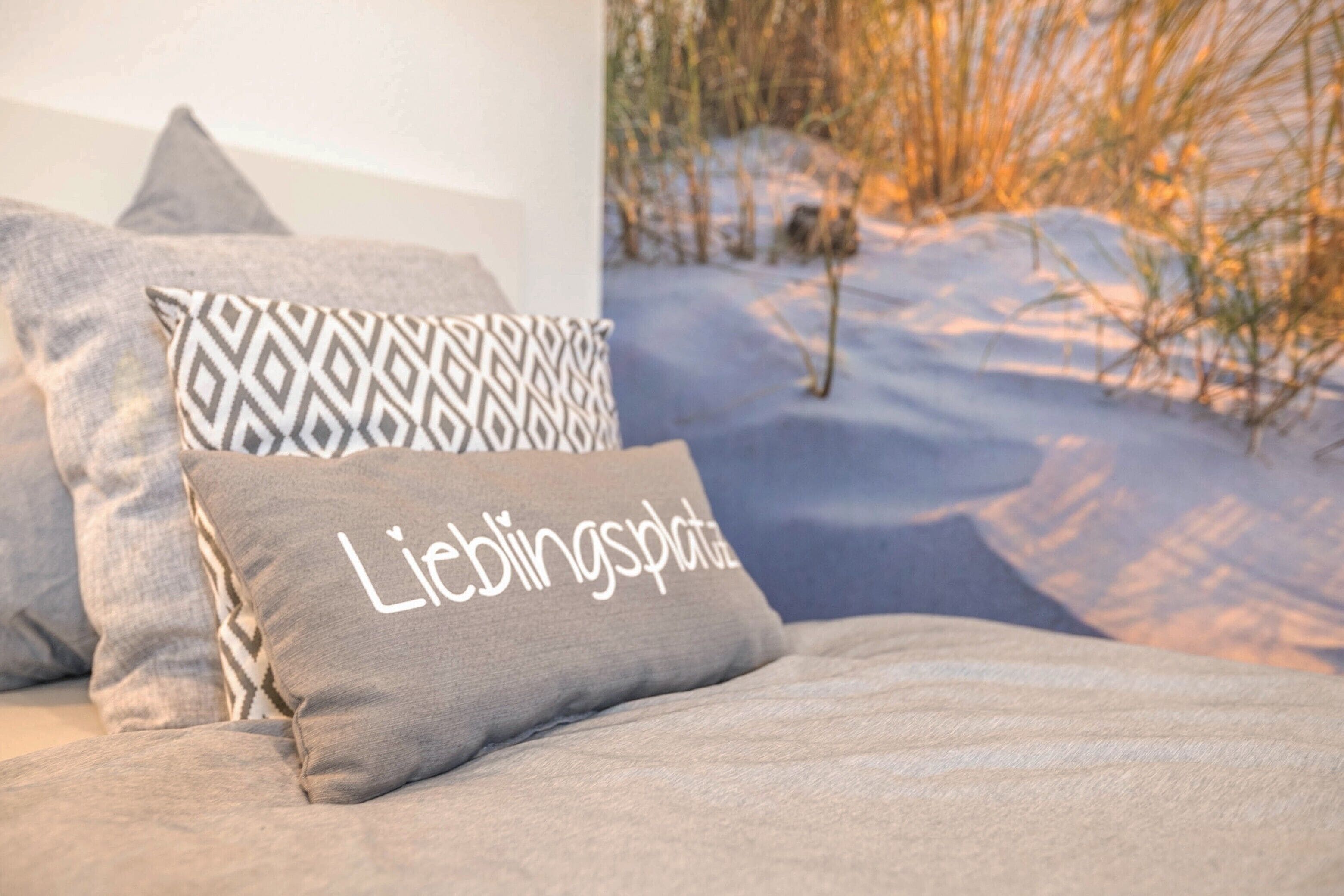 A bed with patterned pillows and a pillow with text, a window with a view of snow and trees.