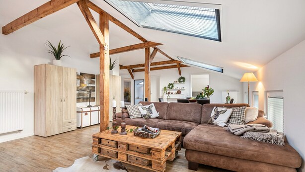 Un loft espacioso con vigas de madera a la vista, un sofá grande, una mesa de centro de madera y un tapete de cuero de vaca.