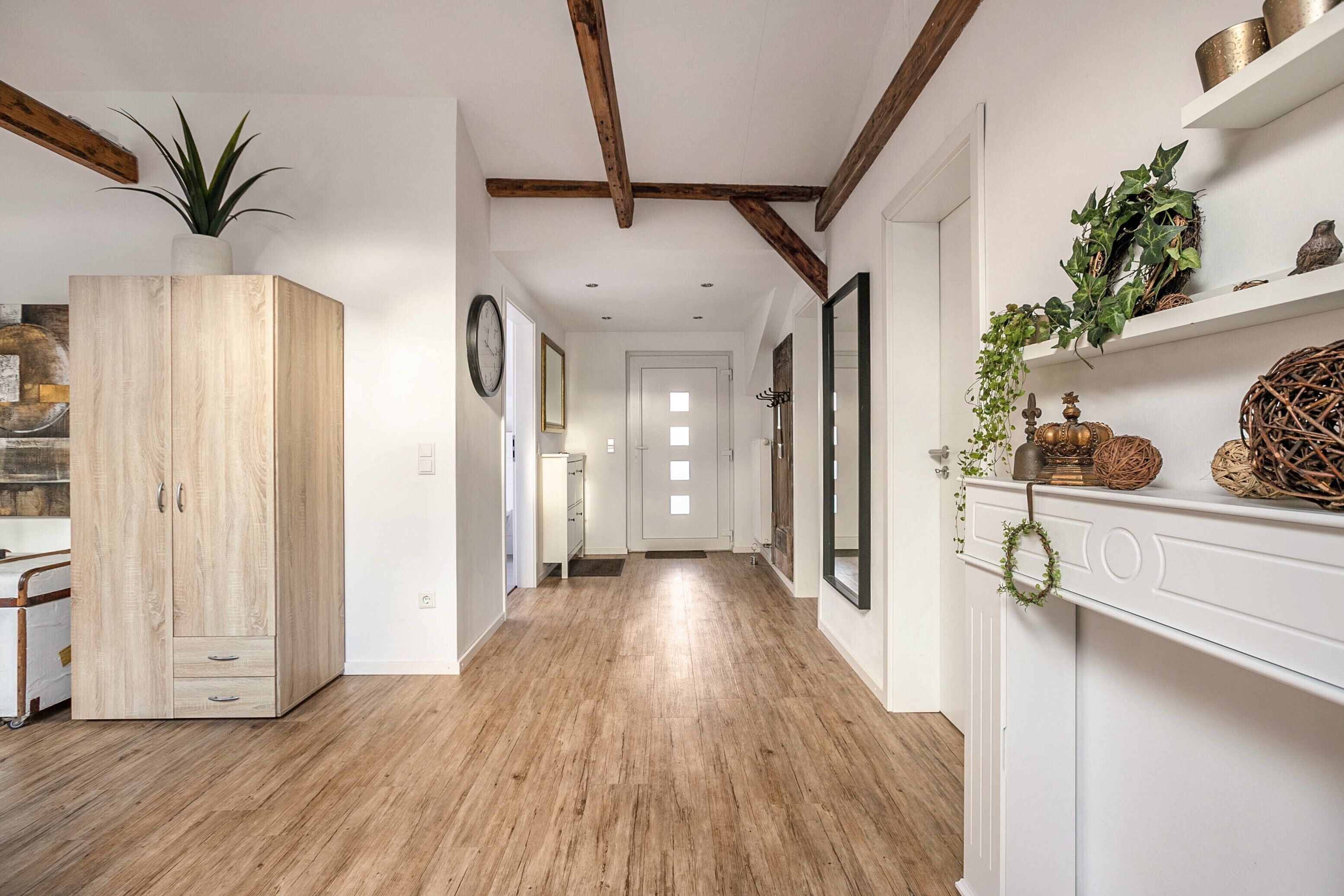 A hallway with wooden flooring, a large cabinet, and a fireplace with decorative items.