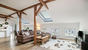 Un loft amplio con vigas de madera expuestas, una cama de altillo, un ventanal grande, un tapiz de cuero de vaca y una zona de estar acogedora.
