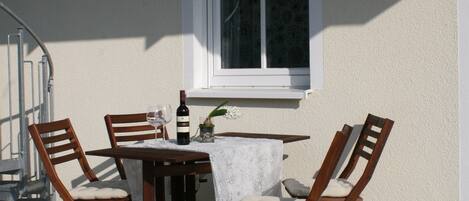 Une terrasse avec une table et des chaises, une bouteille de vin et une fenêtre.