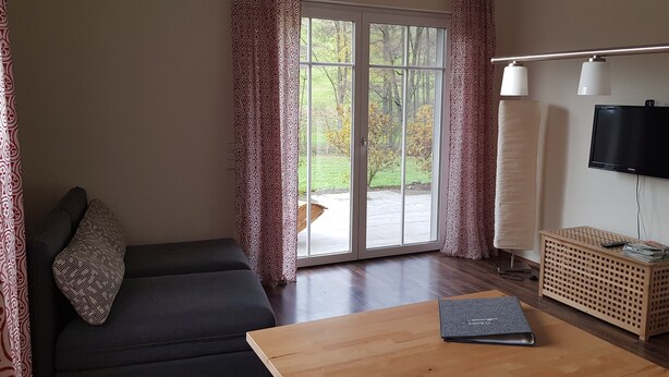 A room with a sofa, a wooden table, a TV, and a sliding glass door leading to a garden. - Apartment 'Ferienwohnung 2' with Private Terrace and Wi-Fi (Sulzbach an der Murr)