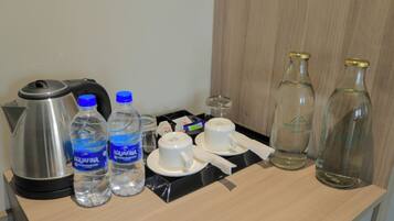 Un plateau de petit-déjeuner dans une chambre d’hôtel, avec une bouilloire, deux bouteilles d’eau, deux tasses blanches, une serviette en papier et deux bouteilles en verre vides.