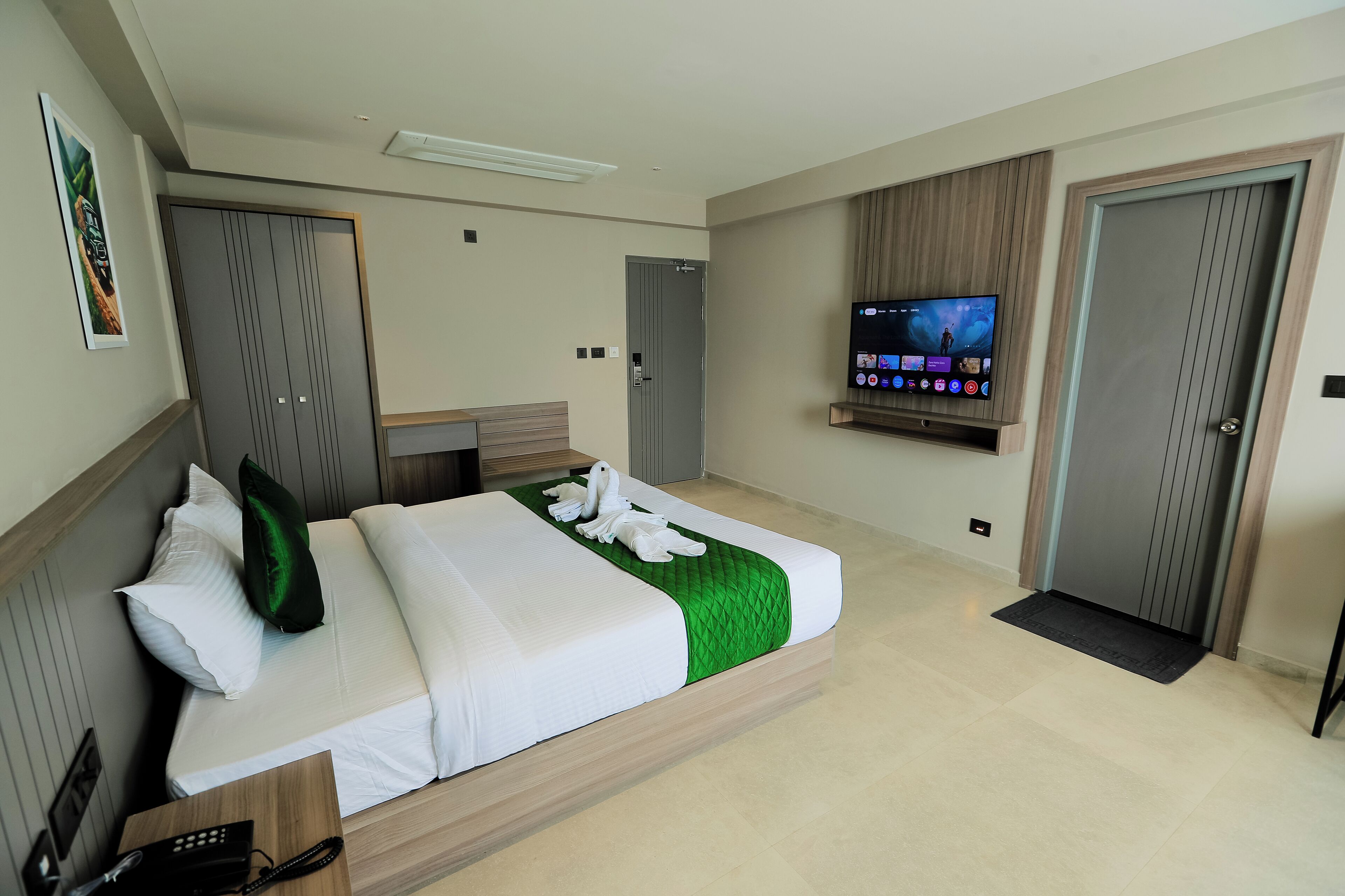 A modern hotel room with a large bed, a flat-screen TV mounted on the wall, and a wooden headboard.
