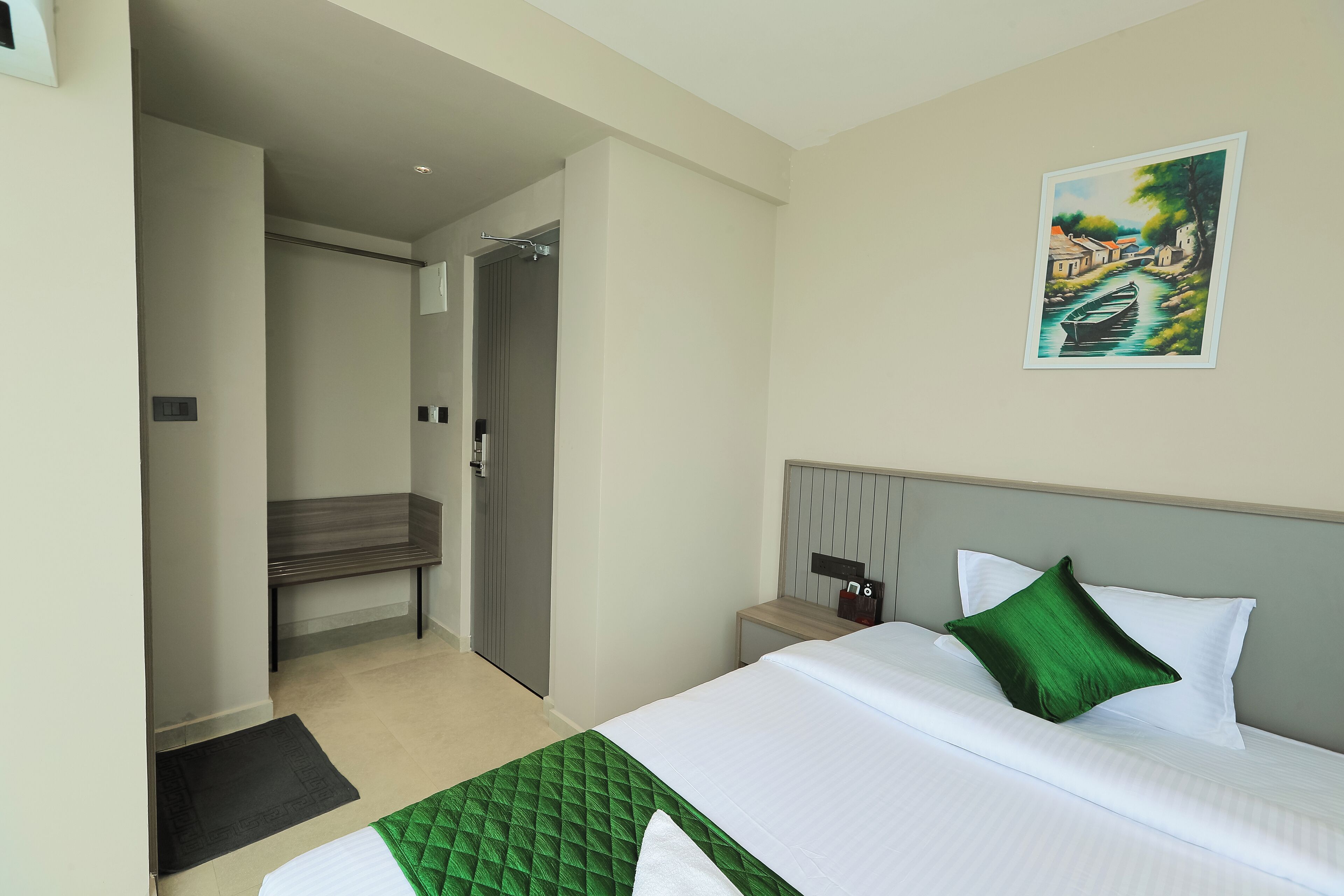 Habitación de hotel con cama, banqueta, mesita de noche y un cuadro en la pared.