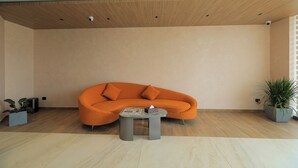 A modern living room with a wooden ceiling, a curved orange sofa, a small round table, and two potted plants. - Mount Land (Sulthan Bathery)