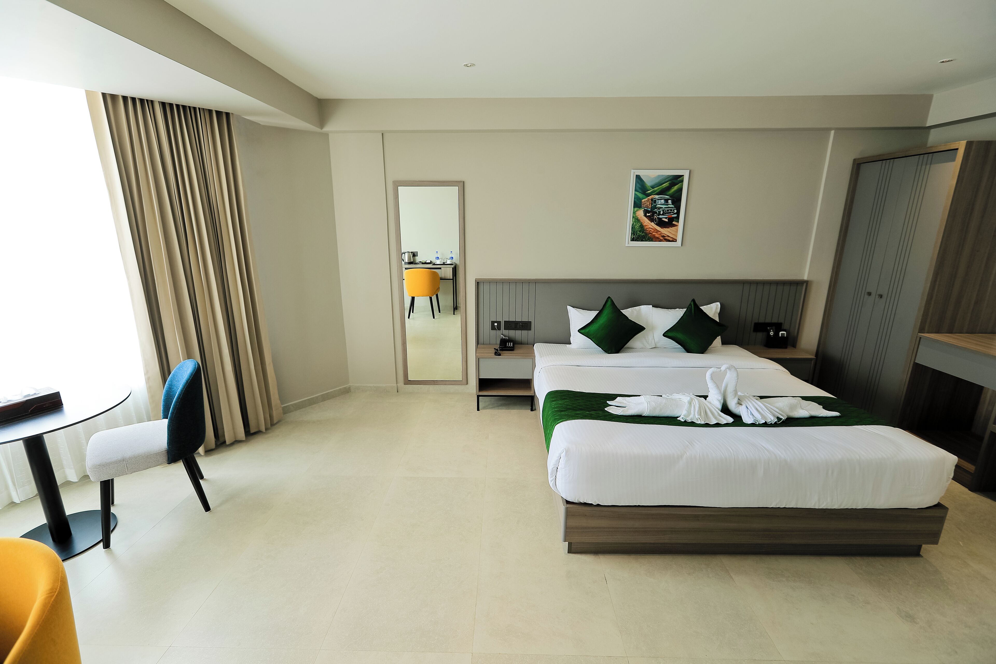 A modern hotel room with a large bed, a desk, a chair, and a dining area.
