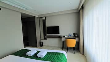 A hotel room with a bed, a desk, a chair, a TV, and a window with curtains.