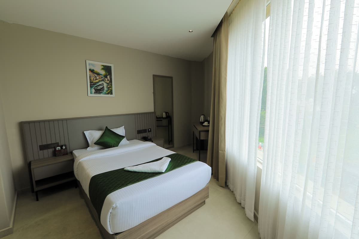 A hotel room with a large bed, a nightstand, a desk, and a window with curtains.