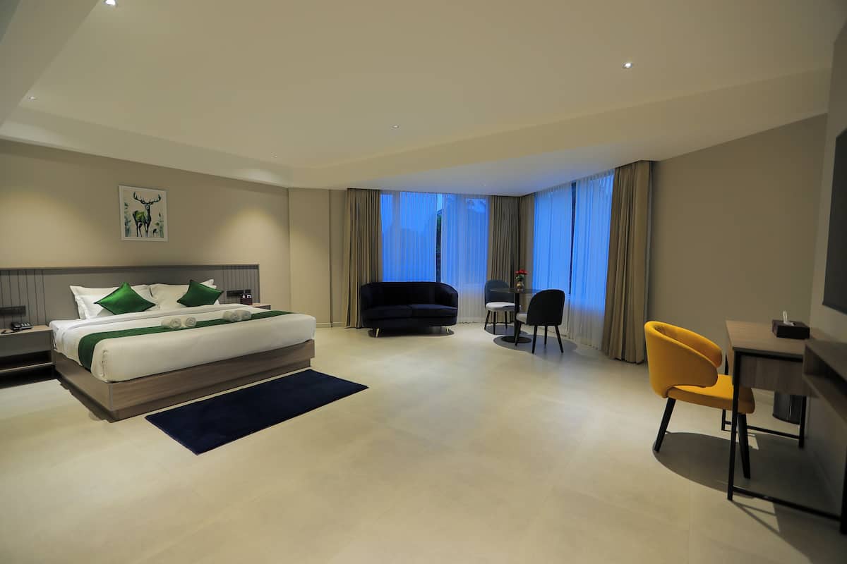 A modern hotel room with a large bed, a sofa, a desk, and a chair.